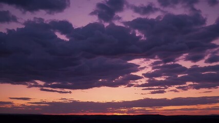 Wall Mural - Stunning 4K time lapse of dark clouds shifting during golden hour where the sky bursts with deep reds and purples before night falls offering a rich visual of light and motion