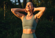 © Abdul - A fit woman with her hands behind her head smiling and looking upwards in a forest setting during golden hour