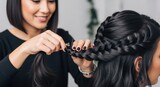 Asian female stylist braiding hair of young asian woman in elegant salon setting