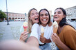 © CarlosBarquero - Three cheerful female friends are enjoying a summer day, taking a selfie while laughing and eating ice cream cones in a picturesque town square