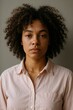 © Ulyana - Young african female with curly hair in a pink shirt against a neutral background