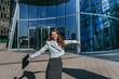© Iona - A stylish woman sits on outdoor steps using a laptop, surrounded by modern glass buildings, embodying a blend of technology and urban elegance.