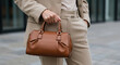 © Aris - Elegant woman carries a brown leather handbag complementing her tailored beige suit ensemble.