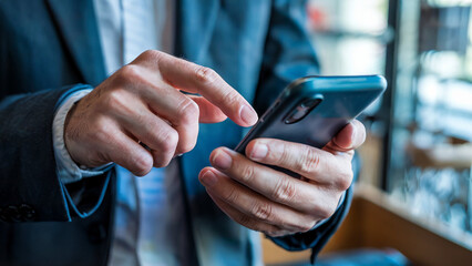 Close up of a businessman in a suit using his smartphone with his fingers touching the screen in a modern office setting