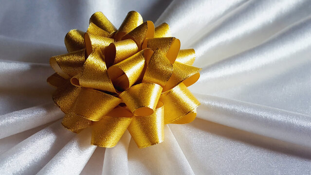 Golden ribbon bow with realistic shadows on white satin background illustration. Ai generated.