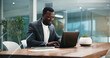 © BuyOutFelix03/peopleimages.com - Business, typing and black man in office, laptop and connection with company website information. African person, employee and consultant in workplace, computer and network with email and internet