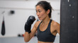 © DOUGLAS - Asian female athlete practicing kickboxing combination in gym, focused and determined expression, wearing sportswear