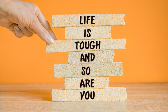Life is tough and so are you symbol. Concept words Life is tough and so are you on brick blocks on a beautiful wooden table, orange background. Businessman hand. Inspirational quote.