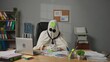 © kinomaster - Halloween businessman ghost in white sheet sits at office desk draws sad face on sticky note and sticks it on forehead. Happy halloween business concept.