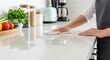 © photoplotnikov - Female cleaning white kitchen counter with fresh vegetables in modern setting