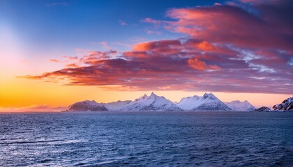 Wall Mural - winter sunrise over a serene ocean landscape with vibrant clouds and snow capped mountains on the distant horizon