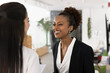 © fizkes - Happy African business woman sharing joyful or humorous moment with female colleague, laughing at joke or personal story, enjoy lighthearted and friendly conversation during break in coworking space