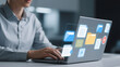 © Maidul - Person typing on laptop with holographic file icons displayed on the screen in a bright office