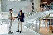 © we.bond.creations - Two businessmen shaking hands in a modern office building lobby, celebrating a successful meeting and solidifying their partnership