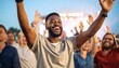 © Cahya - Happy African American man with raised arms cheering at a rock concert, conveying joy and excitement.