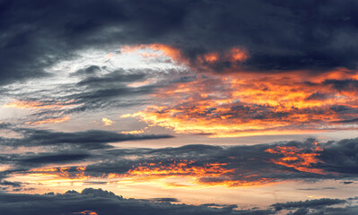 Wall Mural - Dramatic evening sky with glowing orange clouds illuminated by the setting sun against a dark and moody background.