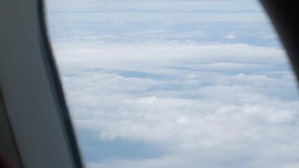 Wall Mural - view through airplane window above the clouds and sky inspiration concept in cinematic aerial flying over white fluffy cloudscape in high altitude sky with fresh clean air and blue skies