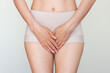 © Ольга Шефер - Young Caucasian woman in beige underwear holding her crotch with her hands. Suffering from severe pain, cystitis, gynecological problems, urinary incontinence. Isolated on a light background.