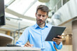 © ty - Smiling busy young employee, young entrepreneur using tablet computer, happy businessman executive looking at tab device analyzing finance trading market data working sitting at office desk.