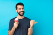 © luismolinero - Young man with a cornet ice cream over isolated blue background pointing to the side to present a product