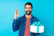 © luismolinero - Young handsome man with a big cake over isolated blue background showing ok sign with fingers