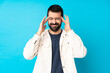 © luismolinero - Young handsome man with white corduroy jacket over isolated blue background with headache
