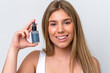 © luismolinero - Young caucasian woman isolated on white background holding a serum while smiling. Close up portrait