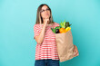 © luismolinero - Young woman holding a grocery shopping bag isolated on blue background and looking up