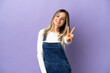 © luismolinero - Young woman over isolated purple background smiling and showing victory sign