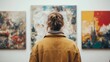 © komgritch - A person with messy hair and a brown jacket observes abstract paintings in an art gallery.