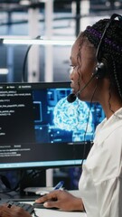 Poster - Vertical video Admin in data center wearing headset assisting users with artificial intelligence troubleshooting. African american woman in server room hub managing support tickets using automated