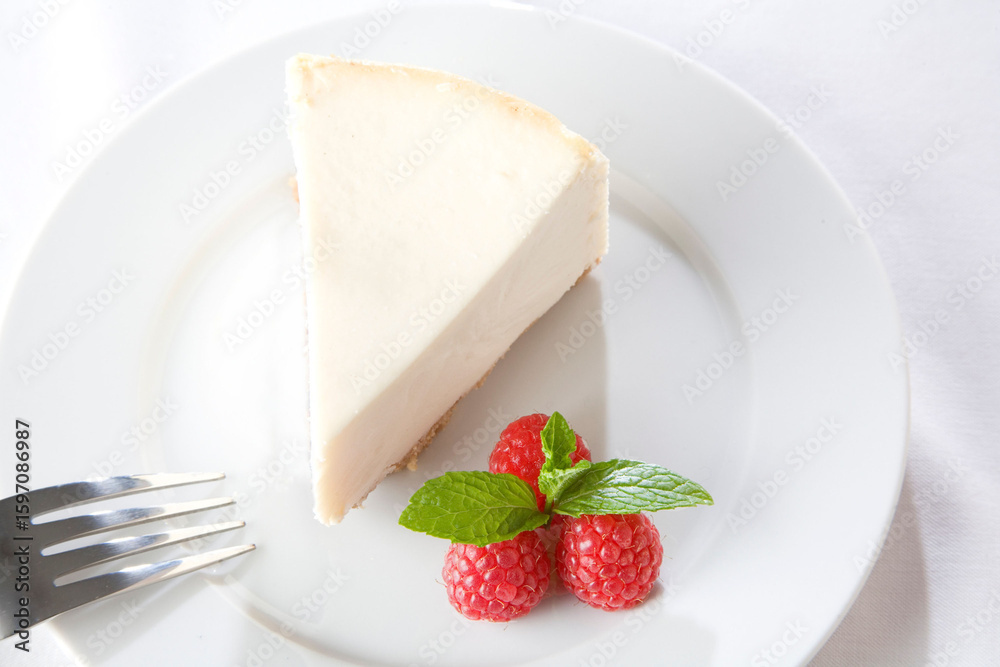 Elegant slice of creamy cheesecake served with fresh raspberries and a mint garnish on a white plate.