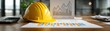 © pingpao - A yellow construction helmet rests on a desk with charts, a calculator, and office supplies, symbolizing project planning and construction management.