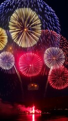 Poster - Brilliant multicolored fireworks explode against a dark sky, with reflections shimmering on the water in the foreground.