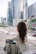 © Moiseii Production - A woman raises her arm while sitting in La Defense business district in Paris facing the skyline and enjoying the city atmosphere