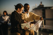 © qunica.com - A group of diverse business colleagues work together on a high tower balcony at sunset, collaborating on documents and projects. The vibrant setting enhances teamwork and innovative discussions.