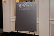 © halcon1 - A black banner at the entrance to a wedding banquet with an invitation for guests. The banner on an easel stands in an elegant interior with the inscription Welcome to our wedding