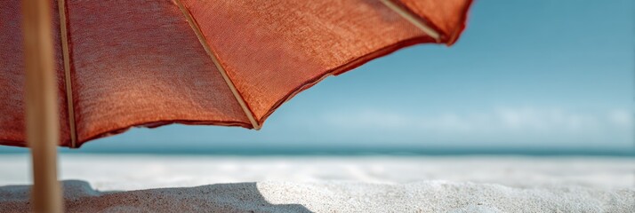 Poster - Red beach umbrella providing shade on a sunny beach with white sand and calm blue sea in the background, creating a perfect relaxing summer vacation atmosphere