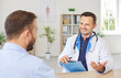 © Studio Romantic - Portrait of a happy smiling young man doctor talking with male patient in office giving recommendations for treatment sitting at the desk in clinic during medical examination. Health care concept.