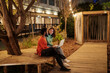 © Studio Marmellata - Happy multiracial male and female friends in casual clothes browsing assignment on netbook while sitting on bench in brightly illuminated park at night in park.