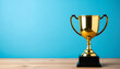 © hardvicore - Gold trophy on wooden table, blue wall background. Winner prize. Close-up.