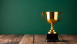 © hardvicore - Gold trophy on wooden table, dark green wall background. Winner prize. Close-up.
