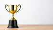 © hardvicore - Gold trophy on wooden table, white wall background. Winner prize. Close-up.