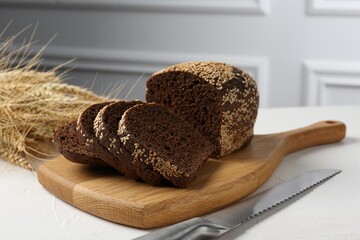Wall Mural - pieces of fresh rye bread with seeds, knife and spikes on white table against light grey wall, close