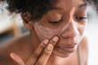 © Studio Marmellata - High angle of charming black female applying purifying mineral mask on face while doing everyday beauty procedure at home