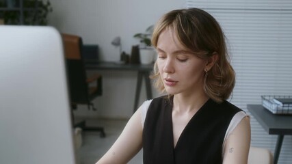 Close up of huge monitor in front of blonde concentrated IT specialist sitting at desk and working in office