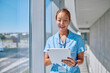 © we.bond.creations - Young Asian female doctor smiling while using a tablet in a modern hospital corridor, embodying professionalism and care in healthcare