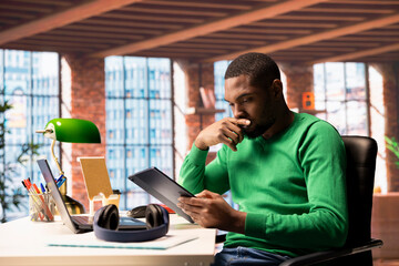 Poster - Remote worker in home office using tablet catching up with emails. African american teleworker reading messages in inbox on device in apartment, thinking of what to reply back