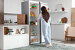 © Pixel-Shot - Beautiful woman taking yoghurt from open fridge in kitchen, back view