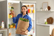 © Pixel-Shot - Young woman with bag of food near open fridge in kitchen